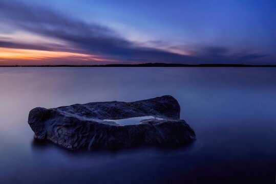 Calm lake with large rock at sunset under colorful sky