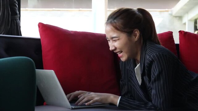 happy young asian businesswoman working on laptop from couch at home, smiling digital nomad enjoying remote work lifestyle, quarter view