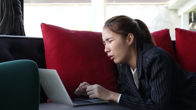 frustrated asian female professional working on sofa during daytime, upset and overwhelmed by technology issues of remote work, quarter view