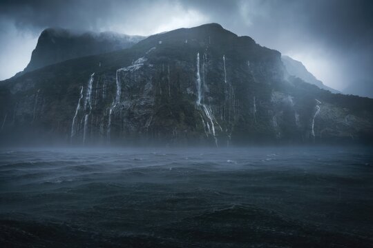 Dark mountain with waterfalls and fog over water scene