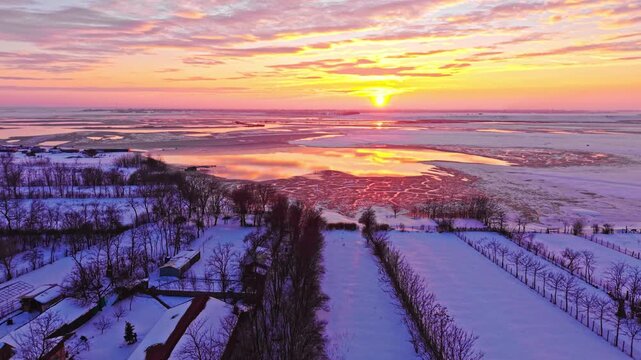 Aerial drone footage of partially frozen lake at golden sunset with snow covered village outskirts, rural Romania, winter