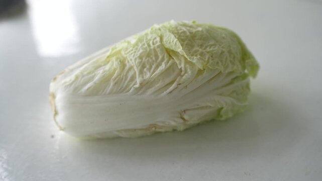 Fresh Napa cabbage placed on a white surface, showcasing its pale green leaves and crisp white stalk. Ideal for themes related to healthy eating, fresh vegetables, cooking ingredients, and agriculture