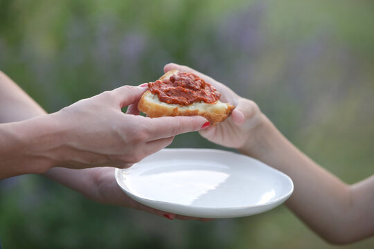 Close-up of woman handing slice of bread with ajvar to child, homemade food, family sharing moment outdoors