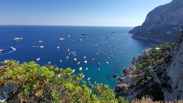 Aerial view of Gardens of Augustus with numerous yachts and boats anchored in the turquoise waters off the coast of Capri, Campania, Italy.