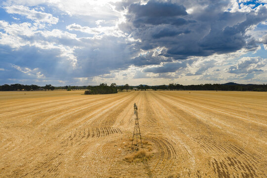 Aerial view of sunshine breaking through clouds over a farm windmill in the middle of a dry paddock