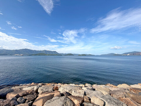 Expansive blue ocean vista with distant mountains and a rocky shoreline under a cloudy sky