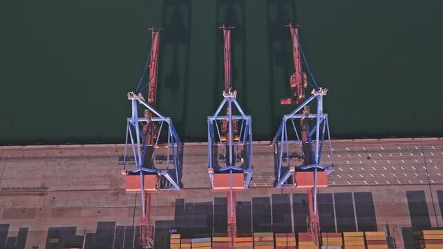 Drone footage of Malaga Port, Spain, pushing forward over three symmetrical gantry cranes straddling the quay edge with dark green water below.