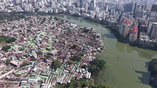 Drone view of a damaged slum section beside a lake and modern city buildings