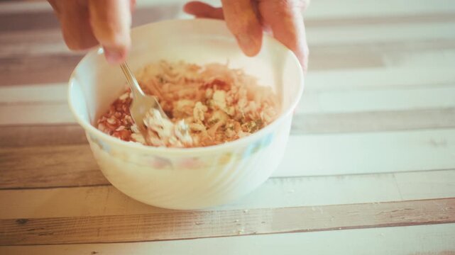 Close-up of chef hands mixing shredded ham, cheese, tomato sauce and dried oregano with a spoon in a bowl. Preparing savory stuffing or topping for homemade pizza and pastry baking, 4k.