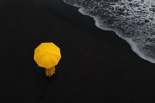 Aerial view of woman with yellow umbrella on black beach
