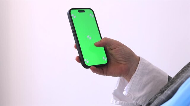 Close-up of senior woman scrolling on smartphone with green screen chroma key display. Mobile app mockup, touchscreen interaction, digital technology and communication concept with copy space.