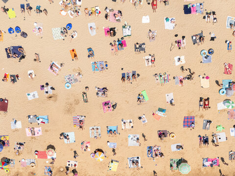 beachgoers sunbathing and relaxing on sandy beach with towels and swimwear, aerial view of relaxed and leisurely vacation scene in blue and tan tones, for travel and vacation.