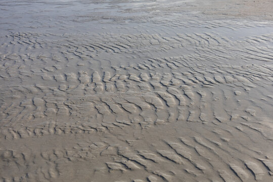 Wet sand shows gentle, ripple-like patterns