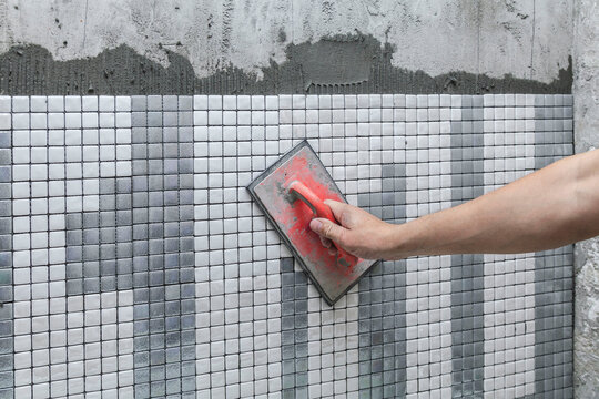 Hand smooths tile adhesive with a red sponge