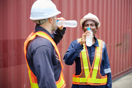 Workers taking a break to drink water. They are standing next to a large shipping container