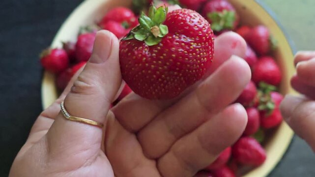 Fresh ripe strawberries in a bowl. The process of removing stems and rinsing the berries in a sieve before making desserts, jam, baked goods, or eating.