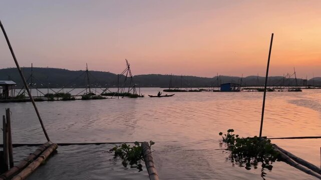 Sunset over a serene lake with boats docked near lush greenery and a distant mountain range