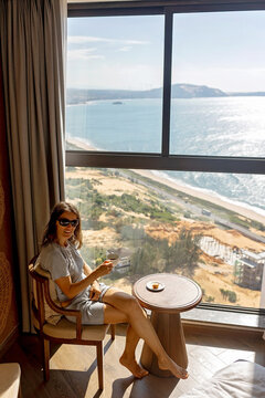 Mother and son in a hotel room, enjoying morning coffee with splendid view over the sea from a top floor