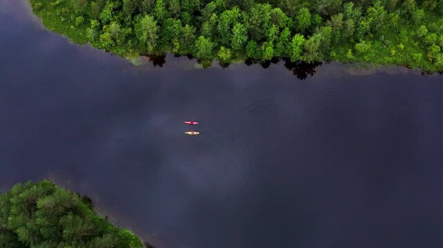Top aerial view of yellow and red kayaks with two people paddling on scenic mountain lake surrounded by pine tree forest in Norway, active summer outdoor travel