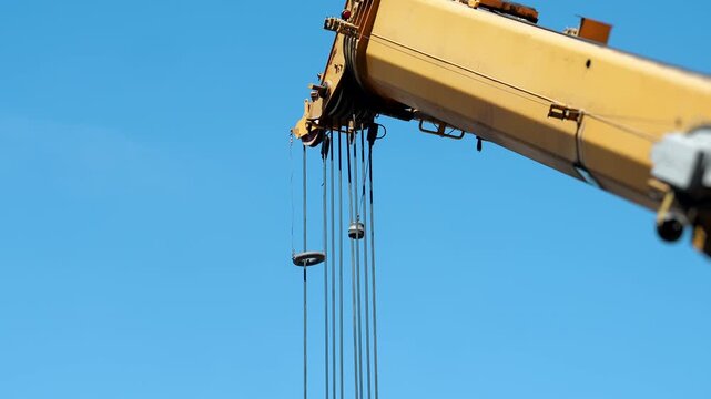 Close-up of a mobile crane boom with steel lifting cables prepared for heavy lifting and industrial construction operations under a clear blue sky.