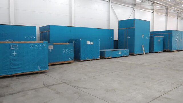 Large industrial equipment wrapped for transportation and stored on pallets inside a modern warehouse ready for shipment and logistics operations.