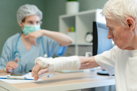 Senior man reaching out to doctor during medical consultation. Elderly patient with bandaged hand seeking professional attention in clinic. Bone fragility and osteoporosis concerns for older