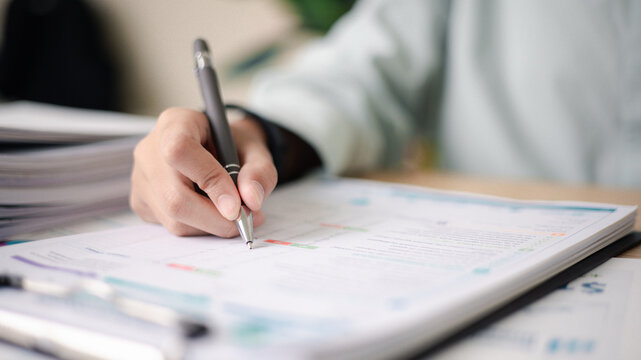 Business professional reviewing performance reports and auditing stack of documents at office desk. Concept of corporate audit, compliance check, data analysis,