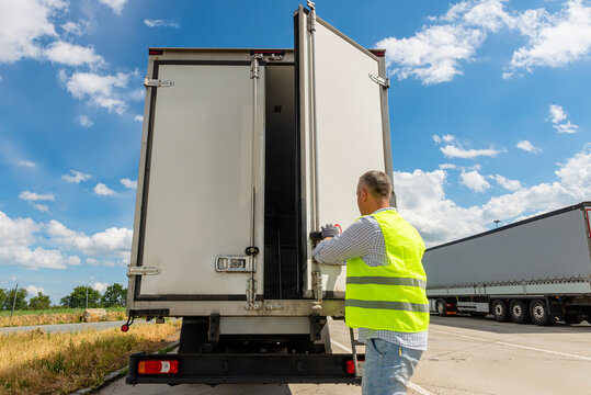 Driver standing near open cargo doors of reefer truck
