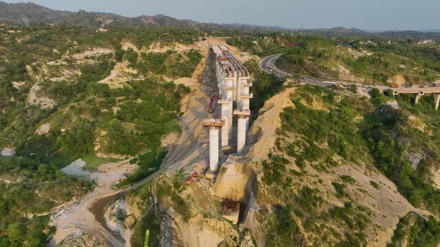 Drone shot across unfinished bridge gap showing construction deck and deep earthworks below.