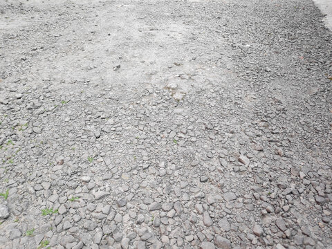 Daylight illuminates a rough textured surface made of countless uneven grey pebble stones together