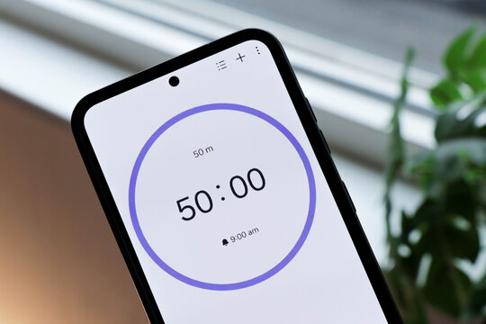 Phone with 50-minute countdown timer to study or be productive, on a interior green, blurry plants background. Productivity, working, studying and active time.
