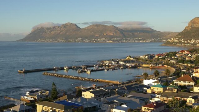 4k 30fps aerial view over Kalk Bay Harbour and the colourful seaside village, looking across the calm waters of False Bay towards Simon's Town on the Cape Peninsula, Western Cape, South Africa.