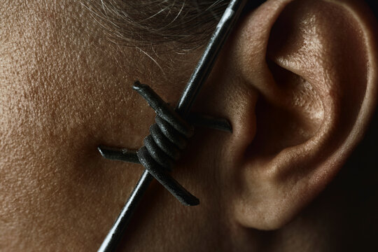 Macro of barbed wire near an ear symbolizing censorship and control