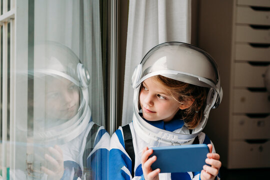 Smiling girl wearing space costume with mobile phone looking at reflection on window