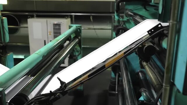 White paper web sheets passing at high speed through green guide rollers and tension bars inside active web offset printing press machine