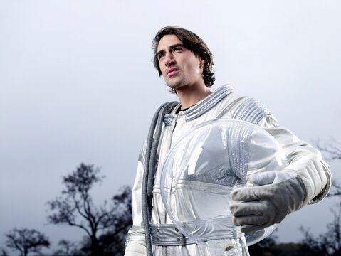 Astronaut in spacesuit holding helmet looking away outdoors