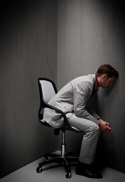 Stressed businessman sitting on chair facing wall in dark corner