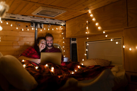 Happy couple watching movie on laptop in illuminated motor home