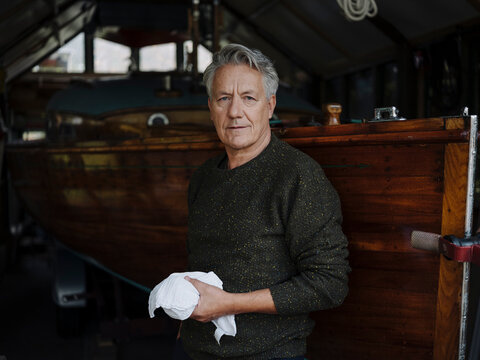 Portrait of a senior man with cloth at wooden boat in a boathouse