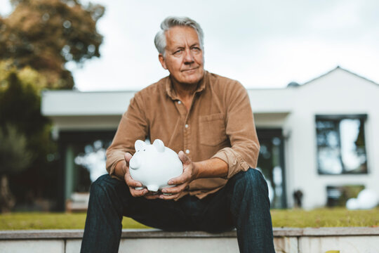 Senior man with white hair holding piggy bank at backyard