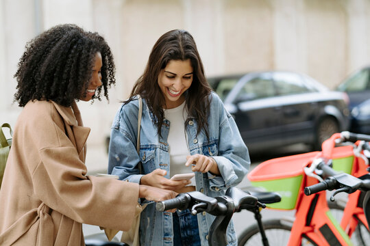 Happy woman with friend paying through smart phone at bicycle parking station