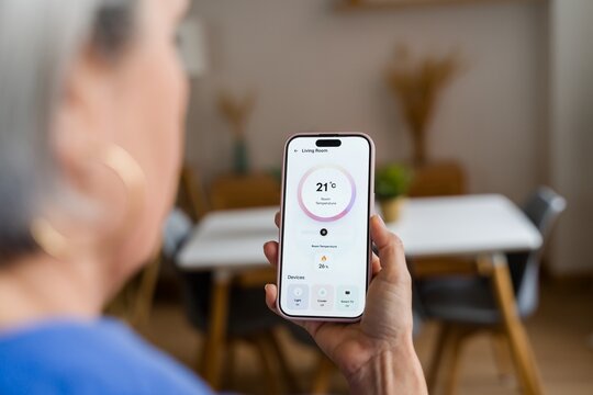 Woman using smartphone app to control smart home thermostat