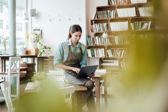 Female cafe owner working on laptop while sitting at table in cafe