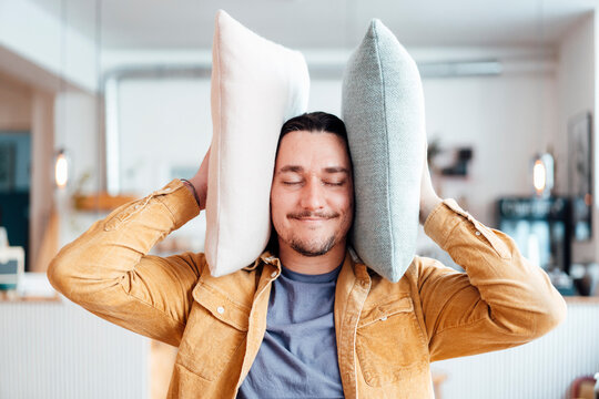 Smiling man covering ears with cushions at cafe