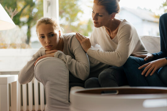 Mother consoling sad teenage girl on couch at home