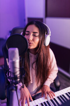 Female musician singing through microphone while playing piano in studio