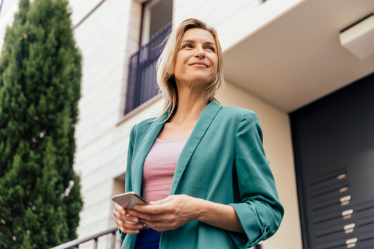 Woman with smart phone in hand at stairs of house looking around