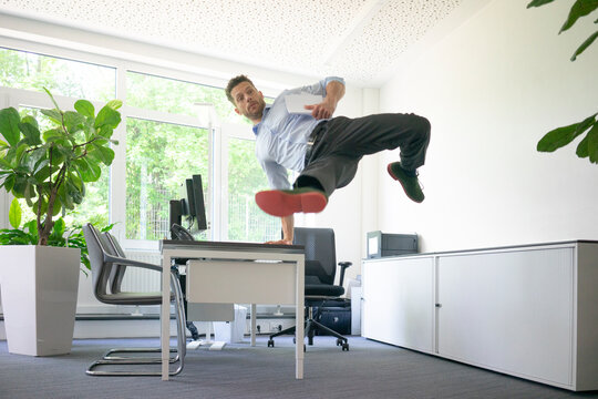 Businessman doing a one-handed handstand on desk in office