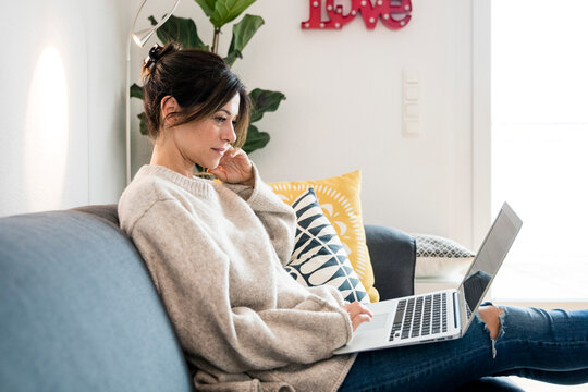 Woman sitting on her couch, surfing the net, using laptop