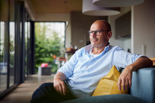 Thoughtful senior man sitting on sofa at home